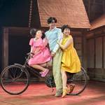 Mei (Victoria Chen), Tatsuo (Dai Tabuchi) and Satsuki (Ami Okumura Jones) all sitting on a bike together and looking back.