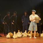 Kanta (Steven Nguyen) wearing a hat and carrying a basket with members of the company behind him with chicken puppets.