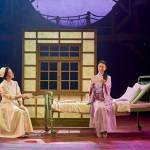 Nurse Emiko (Kumiko Mendl) sitting on a chair and talking to Yasuko (Phyllis Ho), who is sitting on a hospital bed.